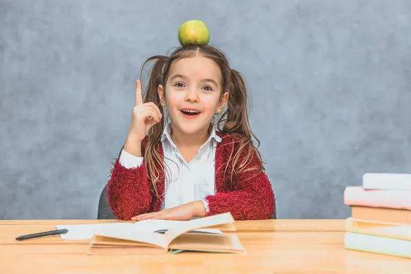 Retrato de linda chica inteligente con manzana en la cabeza. Sentado de una pila de libros en la mesa, una copia del espacio. Concepto de educación y desarrollo . — Foto de Stock