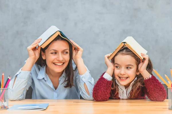 Mãe e filha alegres em um fundo cinza. Durante isso, na cabeça de minha mãe e filha, há livros abertos. Sorrindo olhando em direções diferentes . — Fotografia de Stock