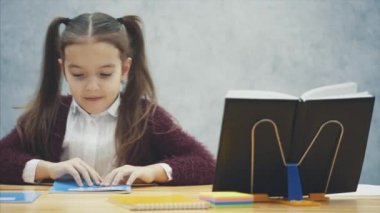 Gri bir kız masaya oturur ve bir defter açar. Zeki, özenli kız öğrenci ödevlerini yapar. Bu yazı sırasında, egzersiz kitapta görünüyor.