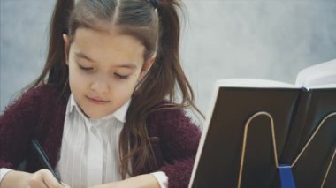 Gri bir arka plan üzerinde akıllı kız öğrenci kapatın. Bu süre zarfında o masada oturuyor. Dikkatle ödev yazıyor.