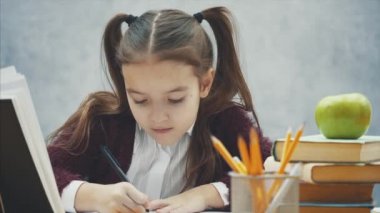 Gri bir arka plan üzerinde akıllı kız öğrenci kapatın. Bu süre zarfında o masada oturuyor. Dikkatle ödev yazıyor.