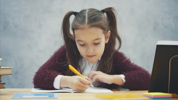 インテリジェントで気配りの女子高生は、テーブルに座りながら宿題を行います。この執筆中に、演習は本の中で見えます. — ストック動画