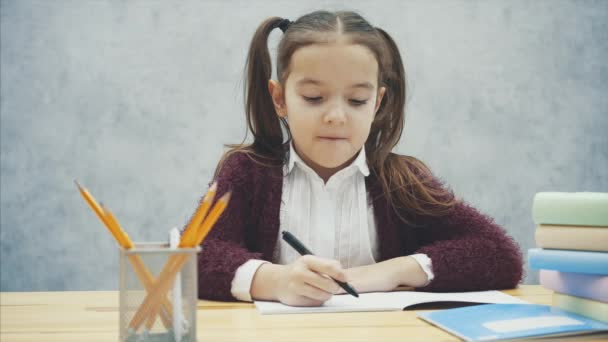 Intelligent Schoolgirl sitter vid bordet. Under detta skriver han en läxa, räkna på en miniräknare. — Stockvideo