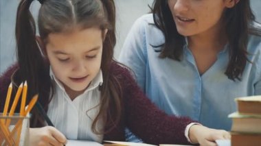 Yakın annem kızımın mutfakta ödevini yapmasına yardım ediyor. Anne ve kızı okuma yla meşguller. Onlar iyi bir ruh hali ve gülümseme vardır.