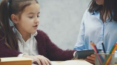 Anne ve kızı siyah bir hesap makinesi ev ödevi güveniyor. Bu sırada gri bir arka plan üzerinde.