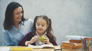 Çalışkan bir kız kitap okur. Annem yeşil bir elma getirdi. Gri bir arka plan üzerinde oturun.