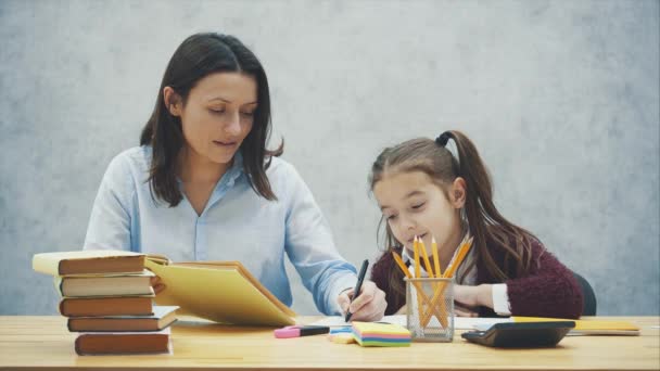 Красивая школьница сидит за столом. Делает домашнее задание с матерью дома . — стоковое видео