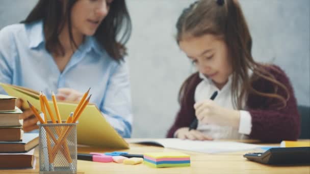 Mooie schoolmeisje zittend aan de tafel. Maakt huiswerk met haar moeder thuis. — Stockvideo