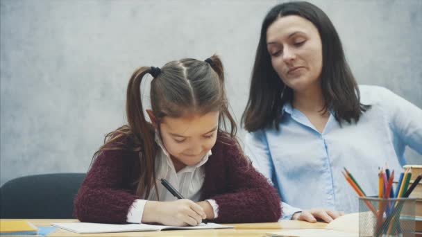 Jovem professor ajudando criança escrita lição ou mãe e filha aprender a escrever, mãe ensinando menina pequena lição de casa isolado em fundo branco, educação estudar casa escola mães dia conceito — Vídeo de Stock