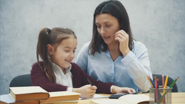 Mamma och dotter räkna med en svart kalkylator läxor. Under detta på en grå bakgrund. — Stockvideo