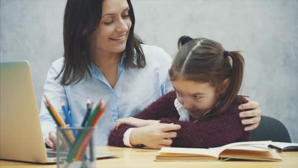 Ung mor och dotter sitter vid bordet på en grå bakgrund. Under detta är en grå laptop tittar. Mamma kramade sin dotter. — Stockvideo