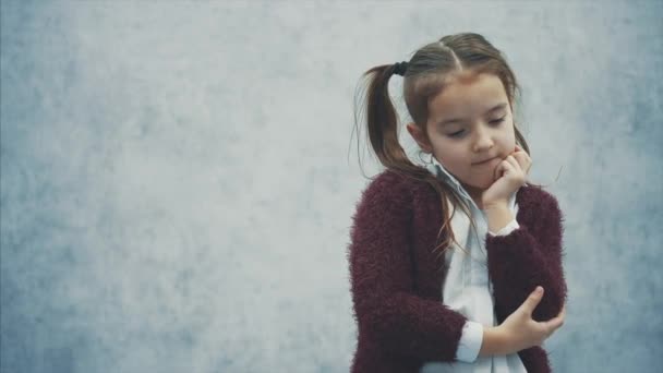 Ein gutes Schulmädchen steht auf einem grauen Hintergrund. Während dieser Zeit hatte sie eine Idee. mit zwei Schwänzen, die eine Hand auf eine Hand legen. — Stockvideo