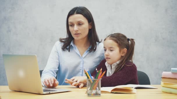 Moeder en tieners meisje met een laptop samen op een grijze achtergrond. Gedurende deze, ze kijken naar de laptop tijdens het chatten. Het kind toont zijn wijsvinger op de monitor. — Stockvideo