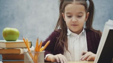 İyi bir kız öğrenci gri bir arka plan üzerinde masada oturur. Bu esnada, bir ödev yapar..