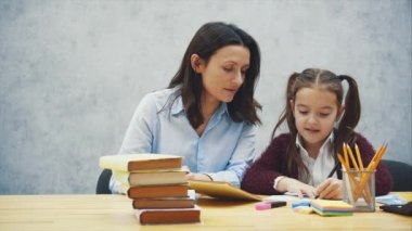 Genç anne bir ders yazmak için çocuk yardım ya da her iki kızı ve anne yazmayı öğrenmek var, küçük bir kız ev ödevi var, gri bir arka plan izole, eğitim, ev okulu, anne