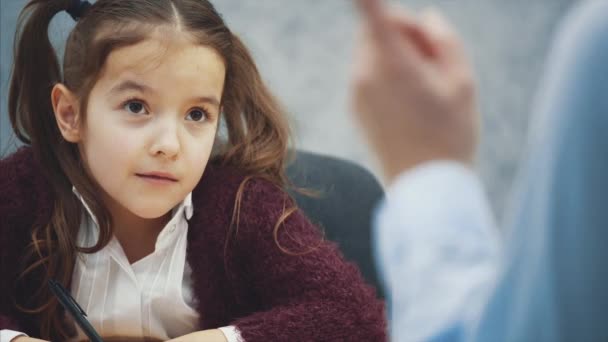 Ein Mädchen auf grauem Hintergrund schreibt Hausaufgaben. während diese Mutter sich streiten und mit der Faust wedeln wird. — Stockvideo