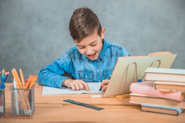 Sevimli okul çocuğu mutlu bir şekilde gülümsüyor, onun copybook heyecan verici bir şey yazıyor.