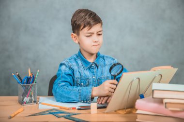 Meraklı küçük çocuk, kitabındadedektif gibi bir şeye büyüteçle bakıyor..