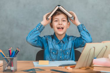 Komik öğrenci kafasına bir çatı gibi kitap koyarak etrafında oynarken, gülümseyerek. Duygular, aptalca davranışlar.