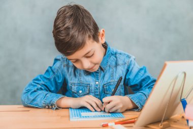 Küçük sevimli okul çocuğu onun copybook imzalayarak, masada oturan.