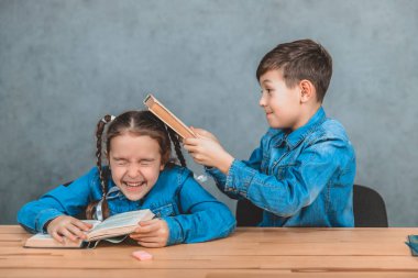 Yaramaz küçük okul çocuğu bir kitap ile kafasında güzel kız öğrenci vuruyor. Mücadele.