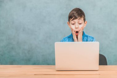 Sevimli küçük okul çocuğu masada oturan, onun laptop gördüğü bir şey tarafından şaşırttı. Açık ağız, yanaklarında eller.