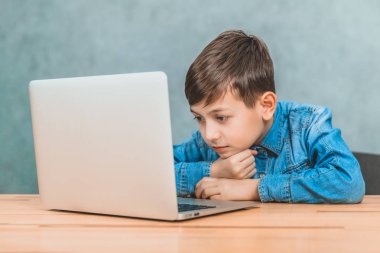 Sevimli küçük okul çocuğu dizüstü bilgisayar ile masada oturan, internette arama.