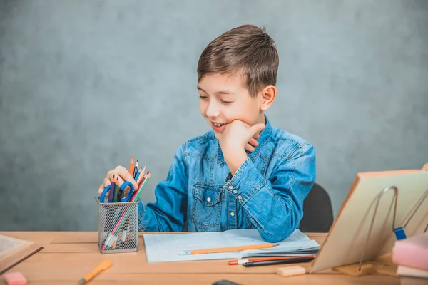 Escolar sonriente eligiendo lápiz colorido de la canasta. Pensando, concentrado . — Foto de Stock