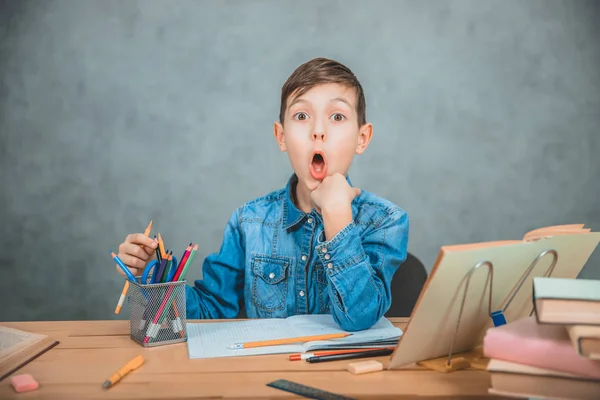 Schoolkid escolhendo lápis colorido da cesta, olhando para a câmera com a boca aberta de forma engraçada . — Fotografia de Stock