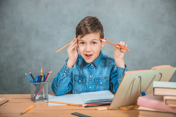 Pequeño niño alegre jugando con lápices durante el proceso de aprendizaje. Montón de libros y especias en el escritorio . — Foto de Stock