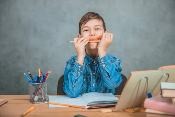 Petit enfant joyeux jouant avec des crayons pendant le processus d'apprentissage. Empilement de livres et de pecilles sur le bureau . — Photo