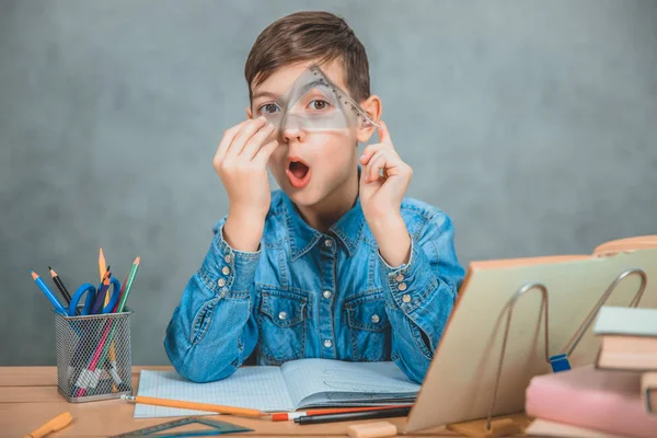 Divertente ragazzino che gioca durante il processo di apprendimento, guardando attraverso il triangolo . — Foto Stock