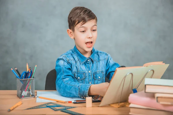 Niño curioso está mirando a través de la lupa en algo en su libro como detective . — Foto de Stock