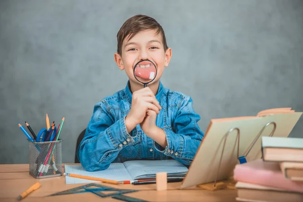 Gracioso colegial jugando con una lupa, sosteniéndola frente a su boca, haciendo ridículas distorsiones. Comportamiento tonto . — Foto de Stock