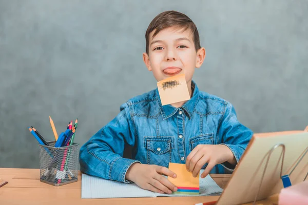 Divertido alumno creativo pegó una pegatina naranja con barba dibujada en su barbilla y mostrar su lengua a la cámara . — Foto de Stock