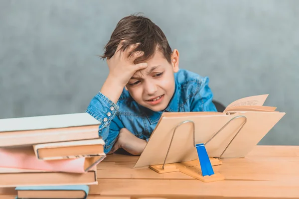 Pequeño alumno lindo no puede resolver la tarea, por lo que se apoyó la cabeza en la mano, pensando difícilmente . — Foto de Stock