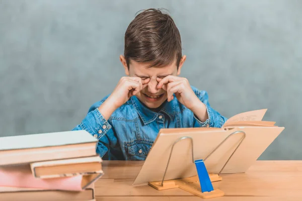 Trött schoolkid gråter, gnugga hans ögon, eftersom han inte vill läsa längre. — Stockfoto