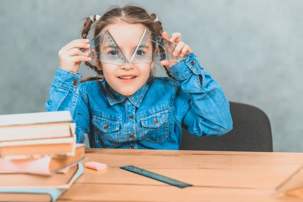 Divertente piccola ragazza curiosa che gioca durante il processo di apprendimento, guardando attraverso due triangoli . — Foto Stock