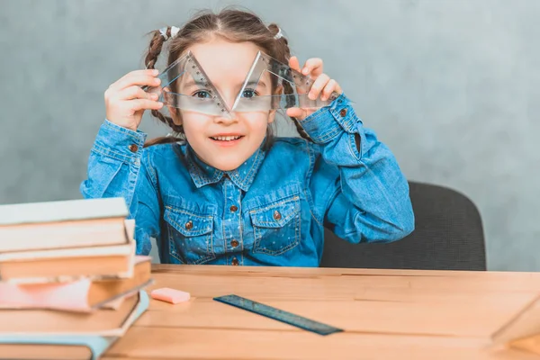 Petite fille curieuse drôle jouant autour pendant le processus d'apprentissage, regardant à travers deux triangle . — Photo