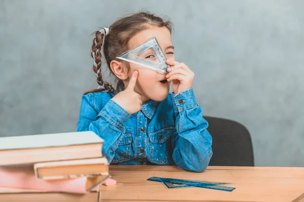 Rolig liten nyfiken flicka leker runt under inlärningsprocessen, tittar genom triangeln. — Stockfoto