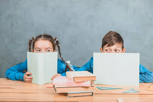 Curious little boy and girl hiding behind the sheets of papers, looking over, at the camera, conspiciuosly. — Stock Photo, Image