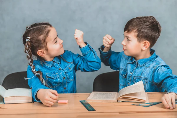 Little funny schoolkids sitting at the table, fighting, shaking their fists. — Stock Photo, Image