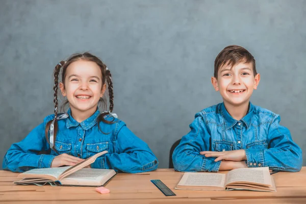 Niños sonrientes inteligentes sentados en el escritorio, libros abiertos, niños sonriendo, con las manos cruzadas . — Foto de Stock