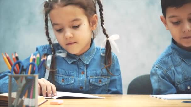 Schulkinder, Bruder und Schwester, sitzen am Tisch und zeichnen. Mädchen mit Zöpfen reicht bunte Penci aus dem verschwommenen Korb auf der Vorderseite. — Stockvideo