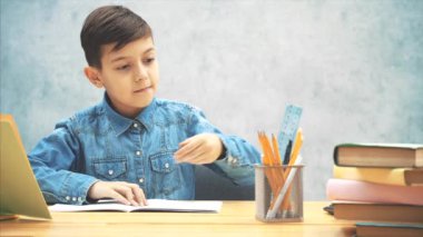 Gri arka planda görünen mavi kot pantolon t-shirt genç konsantre okul çocuk, otururken, bir vurgulayıcı ile yazma.
