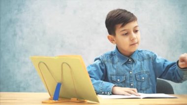 Gri arka planda görünen mavi kot pantolon t-shirt genç konsantre okul çocuk, oturma, copybook açılış, bir vurgulayıcı ile yazma.