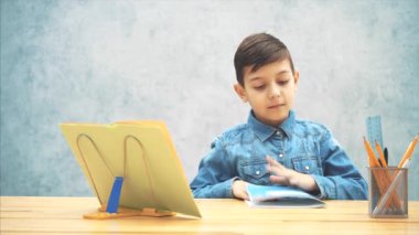 Mavi kot t-shirt genç akıllı okul çocuk yazıyordu, ödevini bitirdi, copybook kapalı ve şimdi sonuç memnun, başparmak işaret.