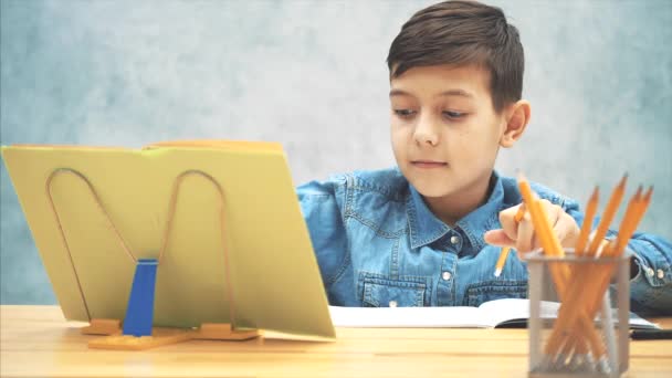 Młode skoncentrowane dziecko szkoły w niebieskim dżinsy t-shirt piśmie, kopiowanie tekstu z książki na bookholder, osiągając linijki, ołówek i podkreślenie. — Wideo stockowe