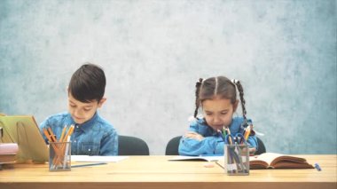 Okul çocukları masada oturuyor, erkek kardeşi yazıyor, kız kardeşi rahatsız oluyor. Yaramaz çocuk karalamalarla kitabını bozdu.