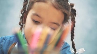 Pigtails ile Sevimli yaratıcı kız sepet ve çizim bir kalem ulaşarak. Ön planda bulanık kalemler.